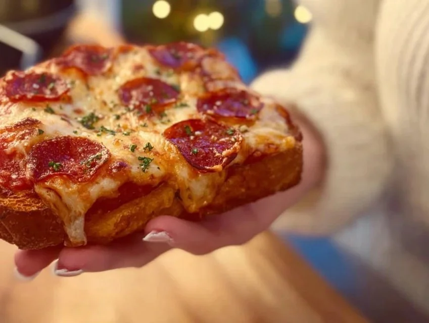 A plate of golden-brown pizza toast topped with cheese, pepperoni, and herbs.